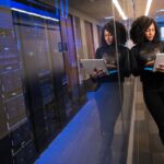 A woman using a laptop navigating a contemporary data center with mirrored servers.