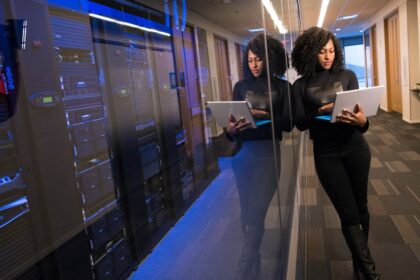 A woman using a laptop navigating a contemporary data center with mirrored servers.