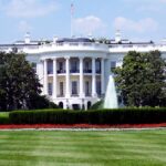 Iconic view of the White House with lush gardens and a central fountain on a sunny day.