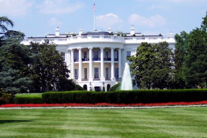 Iconic view of the White House with lush gardens and a central fountain on a sunny day.