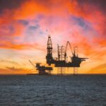 Offshore oil rig silhouetted against a vibrant sunset with dramatic clouds.