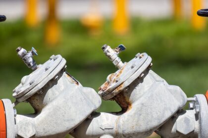Detailed view of rusted industrial gas valves outdoors on a sunny day.