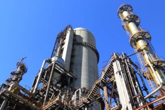 A towering industrial plant under a vivid blue sky, showcasing its intricate architecture and industrial prowess.