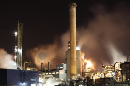 A nighttime view of an industrial factory with smokestacks emitting smoke, highlighting energy production and pollution.