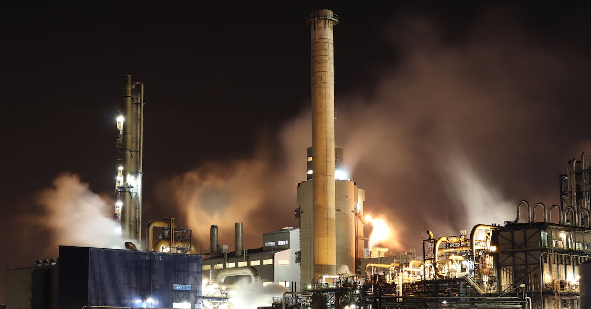 A nighttime view of an industrial factory with smokestacks emitting smoke, highlighting energy production and pollution.