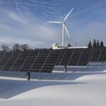 Solar panels and wind turbine in a snowy landscape, showcasing renewable energy sources.