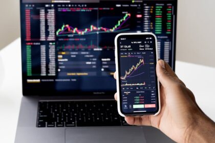 Person checking stock market graphs on laptop and smartphone, focusing on financial data.